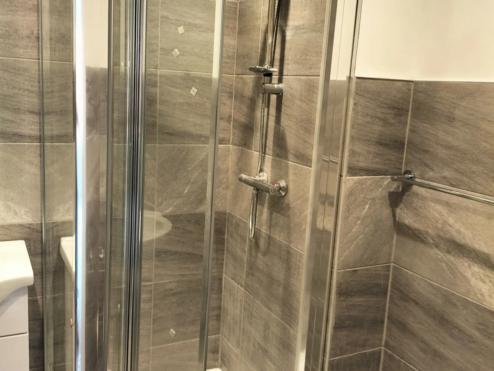 Grey tiled shower room with a glass enclosure and wall mounted shower